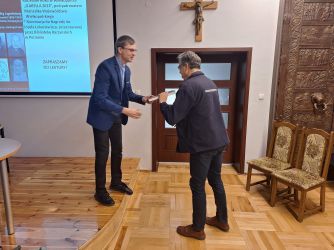 Ks. Łukasz Krucki wręcza egzemplarz publikacji Tomaszowi Janiakowi z MPPP
